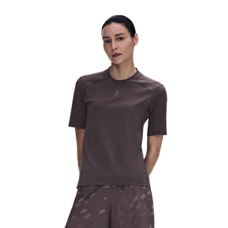 A woman modeling a short-sleeve athletic top in a dark brownish-gray color, paired with matching patterned shorts, against a solid white background. - On Trail-T Solar (Women's) - Mulberry
