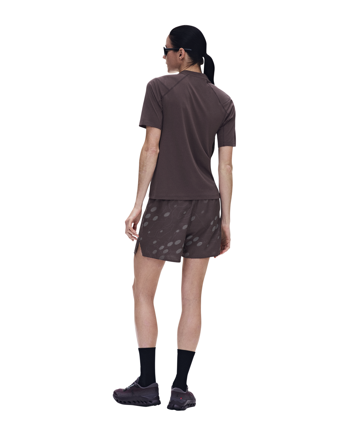 A woman shown from the back wearing a brown short-sleeve athletic shirt and matching brown shorts with a subtle tonal pattern, black socks, and running shoes against a plain white background. - On Trail-T Solar (Women's) - Mulberry