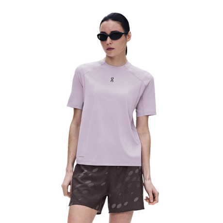 A woman modeling a light purple short-sleeve athletic t-shirt with a small black logo on the chest, paired with dark patterned shorts, against a solid white background. - On Trail-T Solar (Women's) - Foxglove