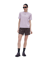 A model wearing a light purple athletic t-shirt, dark brown patterned shorts, black socks, and black running shoes, standing against a solid white background. - On Trail-T Solar (Women's) - Foxglove