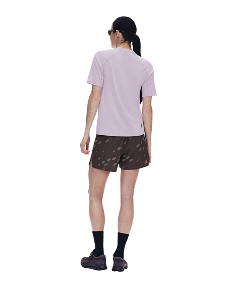 A model shown from the back wearing a light purple short-sleeve athletic shirt, brown patterned running shorts, black socks, and trail running shoes against a solid white background. - On Trail-T Solar (Women's) - Foxglove