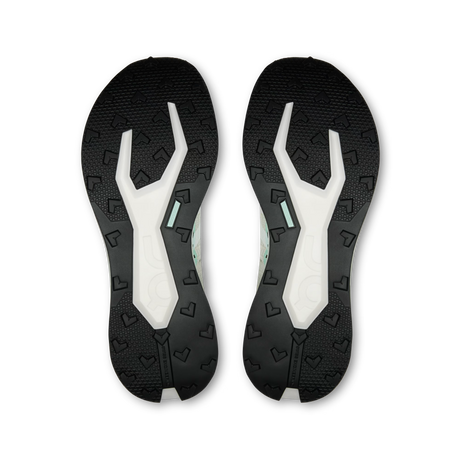 A pair of athletic shoe soles shown from the bottom, featuring a black textured tread with embossed heart-like patterns and a white central channel with a small mint green accent. - On Cloudultra Pro Shoes (Women's) - Ivory/Celeste