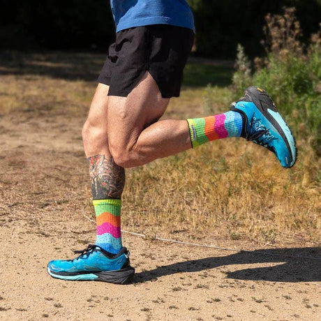 Person running on a dirt path wearing colorful socks and blue running shoes. - Injinji Spectrum Trail Midweight Crew Socks (Unisex) - Sprinkles