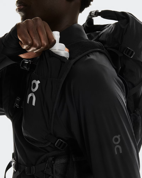 Person wearing a black jacket with a visible brand logo on a light gray background - On Trail Pack 20L - Black
