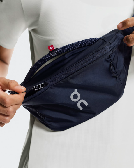 Navy waist bag with 'on' logo held by a person on a light gray background - On Waist Pack 2L Lite - Navy