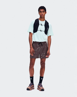 A male model stands against a light gray studio background wearing a white t-shirt, brown patterned shorts, black crew socks, trail running shoes, and a black hydration backpack. - On Trail Shorts (Men's) - Mulberry