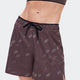 A close-up of a model wearing dark brown athletic shorts with a subtle white topographic pattern and a black drawstring waist, paired with a matching dark brown sports bra against a light gray background. - On Trail Shorts (Women's) - Mulberry