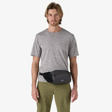 Man wearing a gray t-shirt and green pants with a black waist bag on a white background - Patagonia Terravia Hip Pack 4L - Black