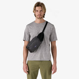 A man wearing a gray t-shirt and olive green pants models a black Patagonia sling bag across his chest against a plain white background. - Patagonia Terravia Hip Pack 4L - Black