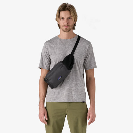 A man wearing a gray t-shirt and olive green pants models a black Patagonia sling bag across his chest against a plain white background. - Patagonia Terravia Hip Pack 4L - Black