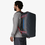Man wearing a gray backpack with red accents and Patagonia logo on a white background - Patagonia Black Hole Duffel 55L - Smolder Blue w/Amanita Red