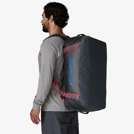 Man wearing a gray backpack with red accents and Patagonia logo on a white background - Patagonia Black Hole Duffel 55L - Smolder Blue w/Amanita Red