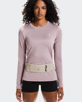 Woman wearing a light purple long-sleeve top and black shorts with a beige waist bag on a white  - On Speed Belt (Unisex) - Fogbackground