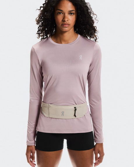 Woman wearing a light purple long-sleeve top and black shorts with a beige waist bag on a white  - On Speed Belt (Unisex) - Fogbackground