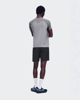 A man shown from the back wearing a light gray athletic t-shirt with dark gray raglan sleeves, black athletic shorts, white socks, and black running shoes with blue accents, against a solid light gray background. - On Performance-T (Men's) - Ember/Ore