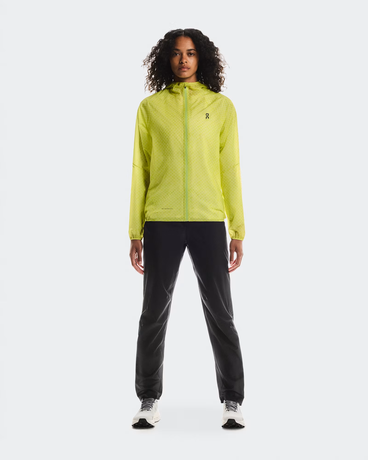 Person wearing a bright yellow jacket and black pants on a white  - On Ultra Jacket (Women's) - Limelight/Limebackground