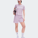 A model wearing a light purple athletic set consisting of a short-sleeve t-shirt, matching shorts, white socks, and white running shoes, holding a matching purple and black bag against a light gray background. - On Performance-T (Women's) - Foxglove/Orchid