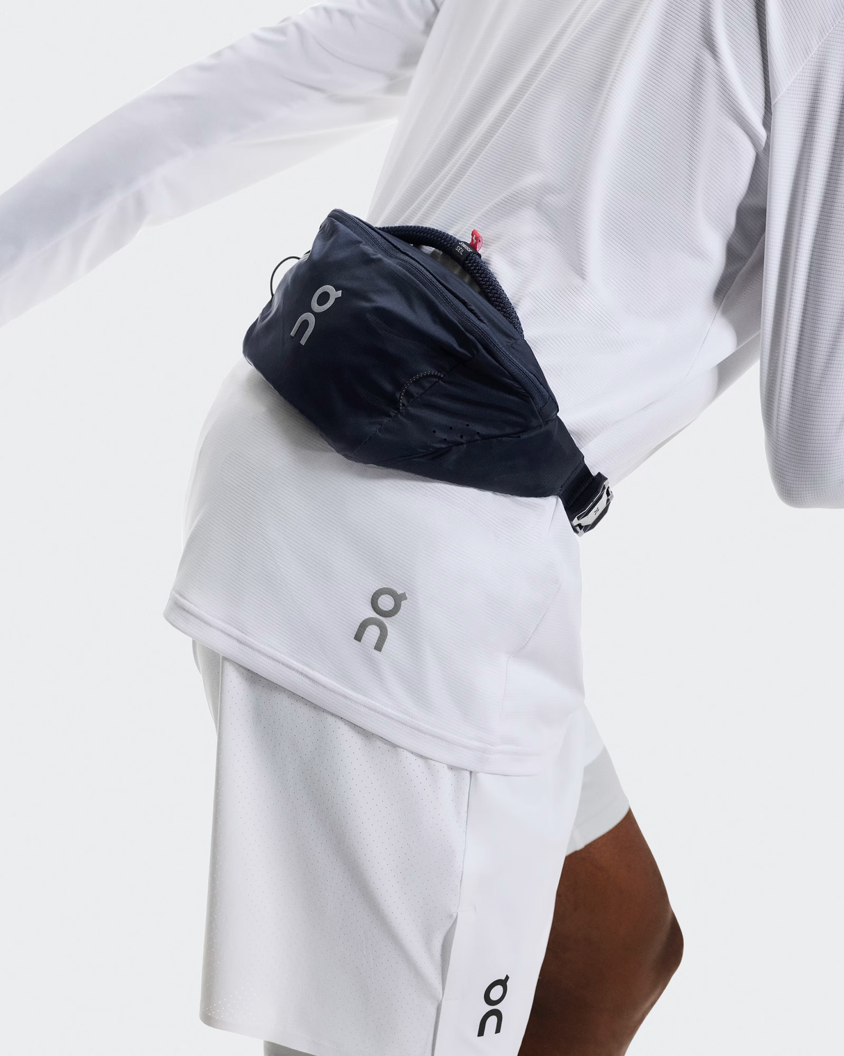 Person wearing a navy waist bag and white athletic outfit with On brand logo. - On Waist Pack 2L Lite - Navy