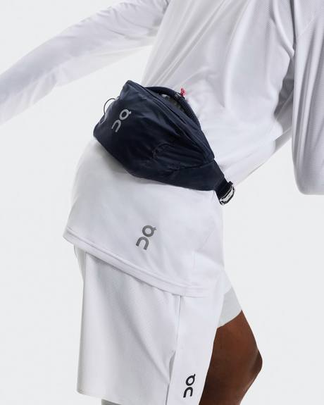 Person wearing a navy waist bag and white athletic outfit with On brand logo. - On Waist Pack 2L Lite - Navy