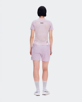 A model viewed from the back wearing a light pink athletic t-shirt and matching light pink shorts, paired with white socks and white sneakers, against a solid white background. - On Performance-T (Women's) - Foxglove/Orchid