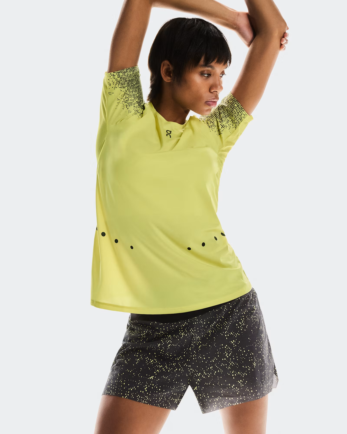 Person wearing a yellow athletic shirt and black shorts with yellow patterns on a white background - On Ultra Shorts (Women's) - Iron/Lime