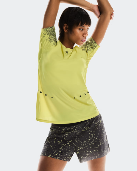 Person wearing a yellow athletic shirt and black shorts with yellow patterns on a white background - On Ultra Shorts (Women's) - Iron/Lime