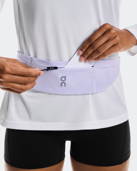 Person wearing a white shirt and black shorts with a purple running belt featuring a brand logo. - On Speed Belt (Unisex) - Thistle