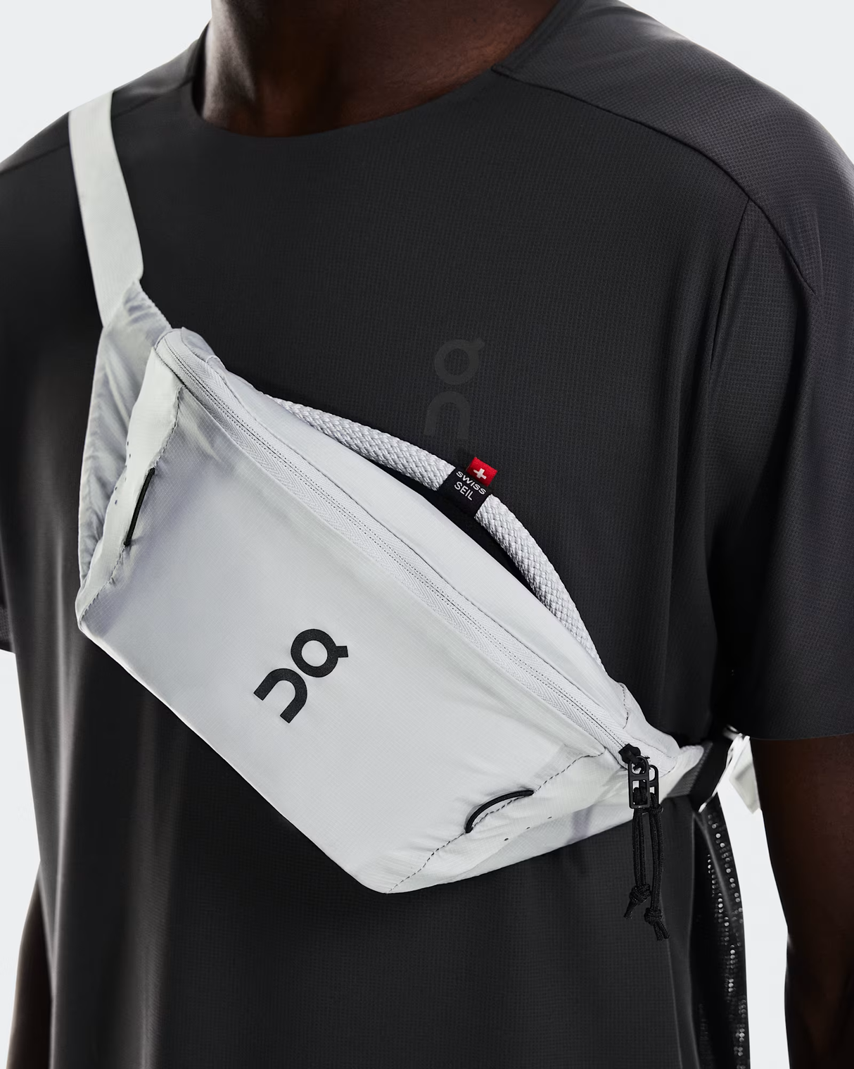 Person wearing a gray waist bag with a brand logo on a plain background - On Waist Pack 2L Lite - Glacier