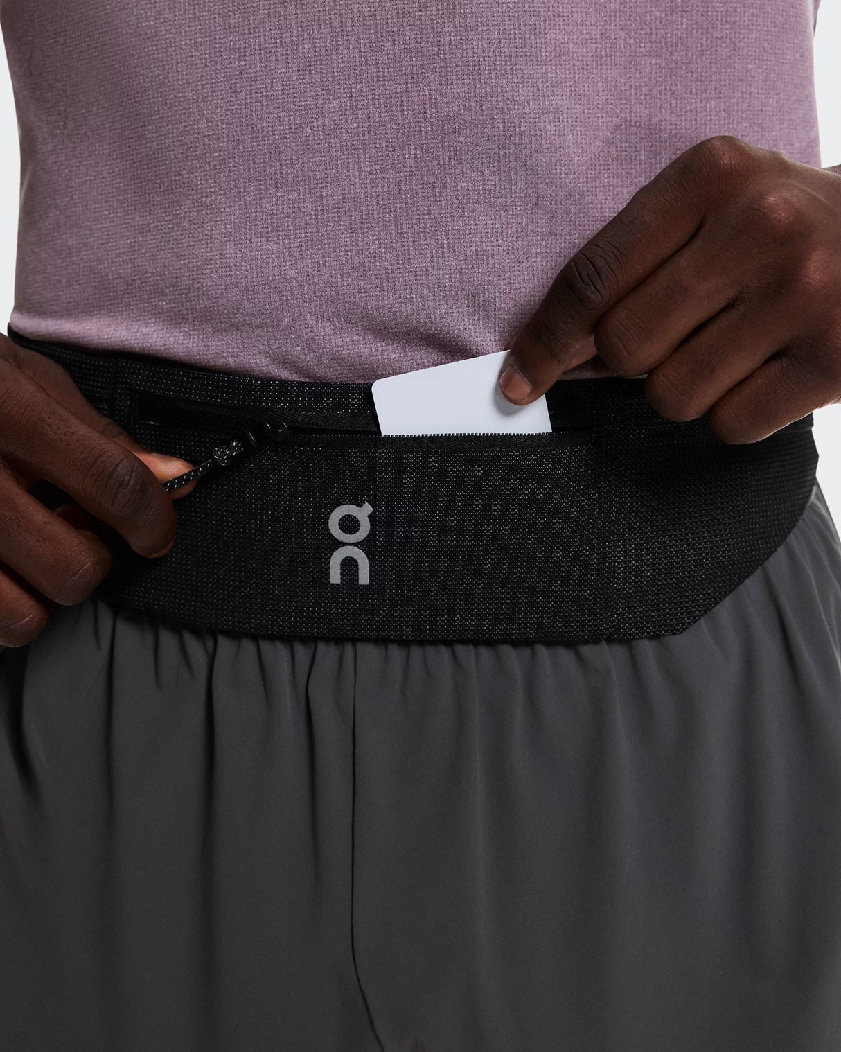Person wearing a black waist bag with a visible brand logo, holding a white card. - On Speed Belt (Unisex) - Black