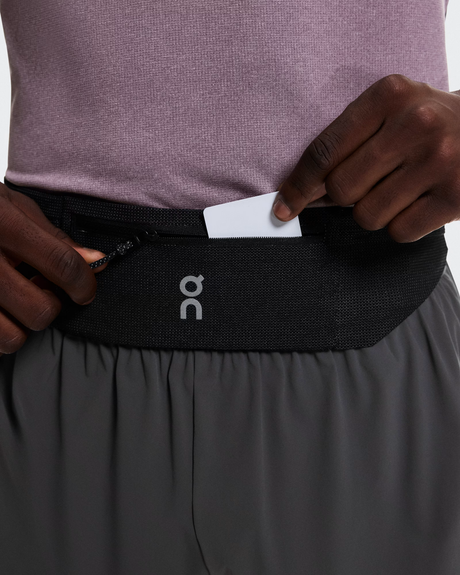 Person wearing a black waist bag with a visible brand logo, holding a white card. - On Speed Belt (Unisex) - Black