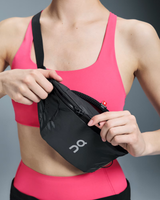 Person wearing a pink sports bra and shorts, holding a black waist bag with a brand logo. - On Waist Pack 2L Lite - Magnet