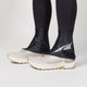 Black ankle covers worn over white running shoes on a light gray background - Altra Trail Gaiters - Black/Silver/Grey