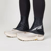 Black ankle covers worn over white running shoes on a light gray background - Altra Trail Gaiters - Black/Silver/Grey