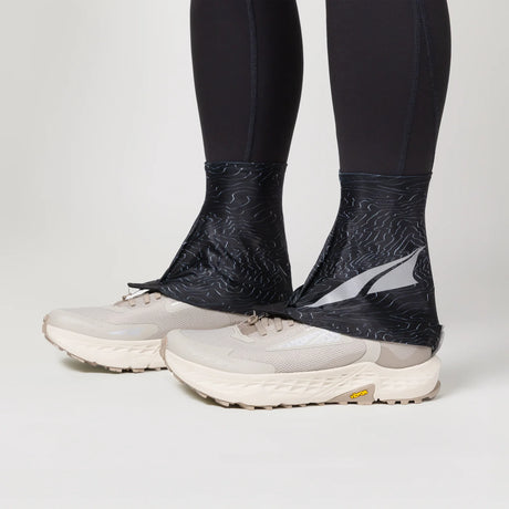 Black ankle covers worn over white running shoes on a light gray background - Altra Trail Gaiters - Black/Silver/Grey