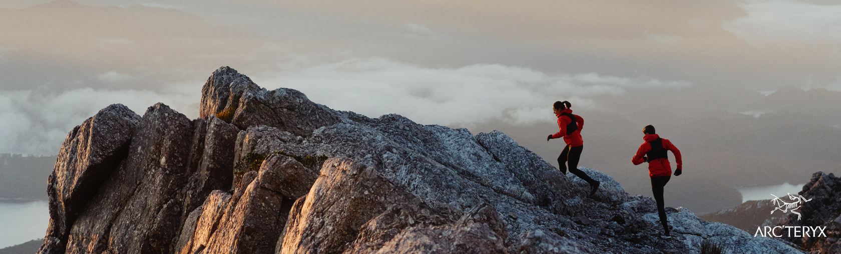 Two people trail running or skyrruning on a rocky mountain in tasmania with a cloudy sky.
