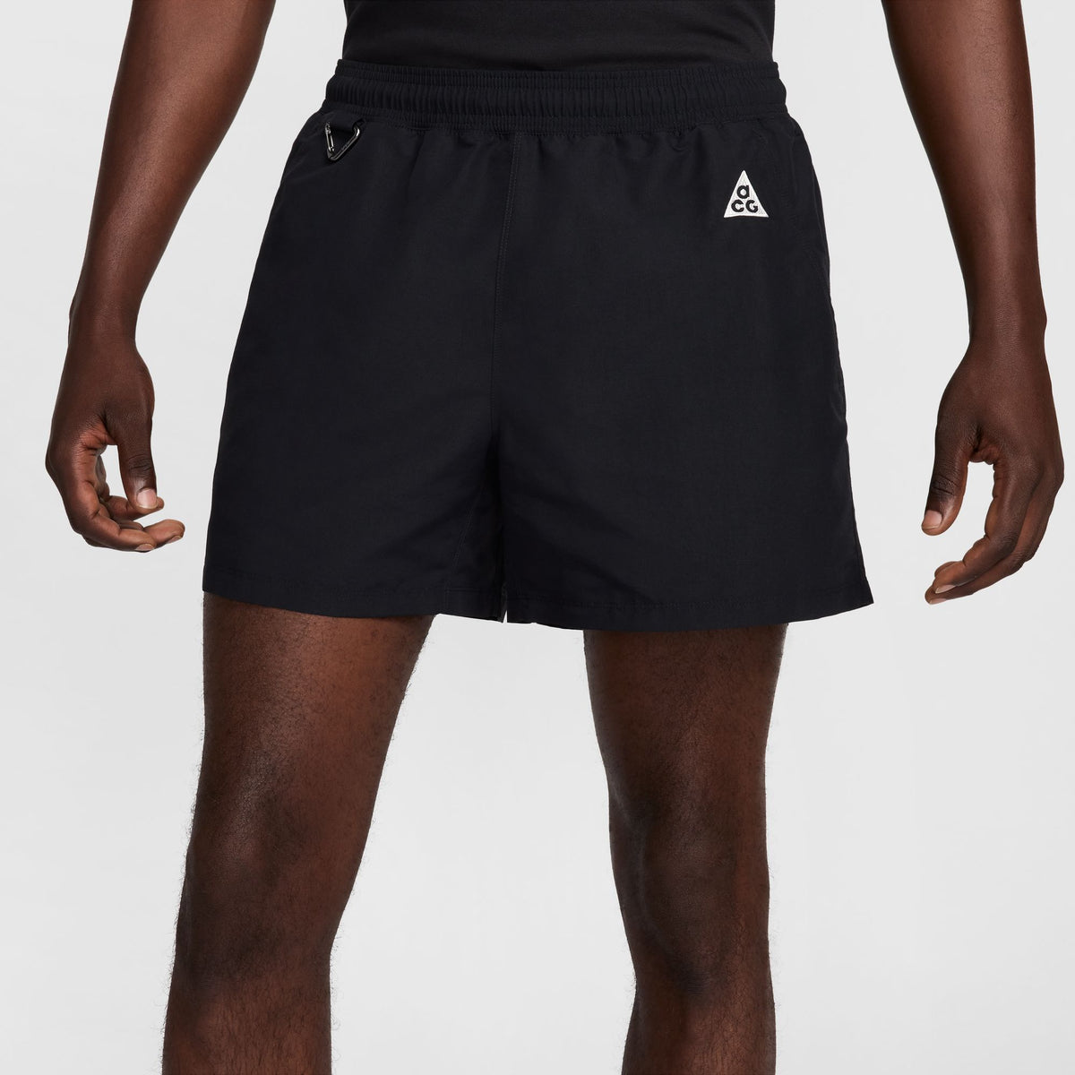 Black athletic shorts with an elastic waistband, side pockets, and a small white geometric logo on the left hip, shown on a model against a light gray background. - Nike ACG Reservoir Goat Shorts (Men's) - Black/Anthracite/Summit White
