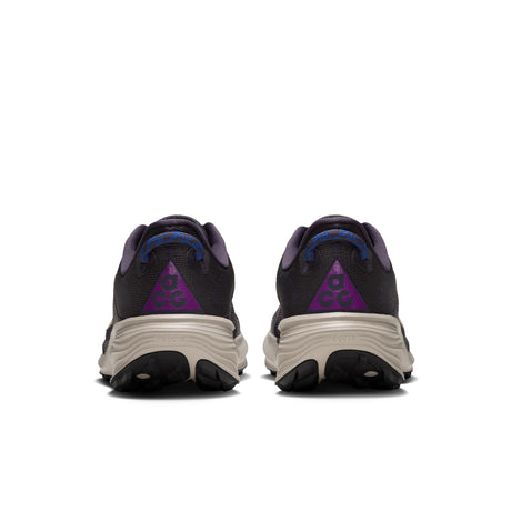 A pair of trail running shoes shown from the rear, featuring a black mesh upper, a purple triangular logo on the heel, and a chunky beige midsole. - Nike ACG Pegasus Trail Shoes (Men's) - Gridiron/Cream II-Racer Blue