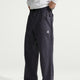 A person wearing dark charcoal gray technical cargo pants with a small white ACG logo on the pocket, paired with a white shirt, shown from the waist down against a light gray studio background. - Nike ACG Dolomiti Pants (Men's) - Gridiron/Summit White