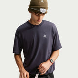 A man wearing a dark navy crewneck t-shirt with a small white geometric triangle logo on the left chest, styled with a brown beanie and a headlamp. - Nike ACG Dri-FIT T-Shirt (Men's) - Gridiron