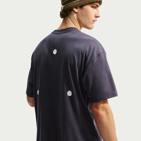 A man wearing a dark navy blue oversized t-shirt with three white circular cutouts on the back, paired with a brown knit beanie, shown from a three-quarters back view against a light gray background. - Nike ACG Dri-FIT T-Shirt (Men's) - Gridiron
