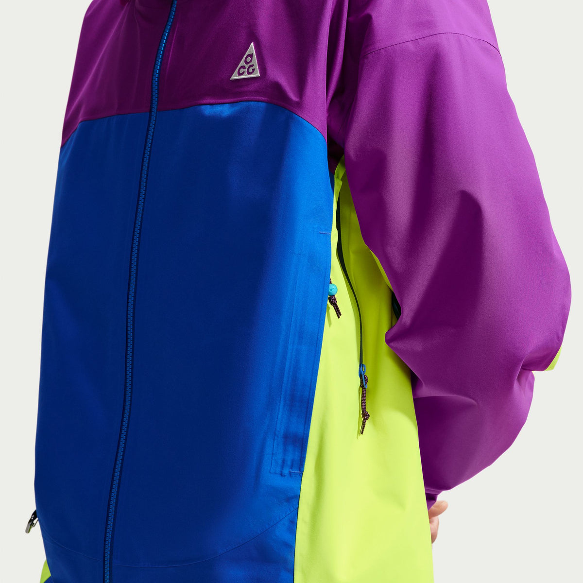 A close-up of a colorblock ski jacket featuring a purple upper section and sleeve, a royal blue front panel, and a neon yellow-green side panel. A small white triangular G-1000 logo is visible on the chest. - Nike ACG Misery Ridge Storm-FIT ADV GORE-TEX Jacket (Men's) - Bold Berry/Hyper Royal/Lemon Venom