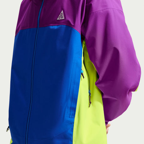 A close-up of a colorblock ski jacket featuring a purple upper section and sleeve, a royal blue front panel, and a neon yellow-green side panel. A small white triangular G-1000 logo is visible on the chest. - Nike ACG Misery Ridge Storm-FIT ADV GORE-TEX Jacket (Men's) - Bold Berry/Hyper Royal/Lemon Venom