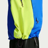 Close-up of a Nike windbreaker jacket with a color-blocked design featuring neon yellow, royal blue, and dark blue panels, with a drawstring hem and a small white swoosh logo. - Nike ACG Misery Ridge Storm-FIT ADV GORE-TEX Jacket (Men's) - Bold Berry/Hyper Royal/Lemon Venom