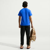 A man is shown from behind wearing a bright blue athletic t-shirt, black pants, and hiking shoes while carrying a beige backpack against a clean white studio background. - Nike ACG Dri-FIT Short-Sleeve Base Layer Top (Men's) - Hyper Royal/Summit White