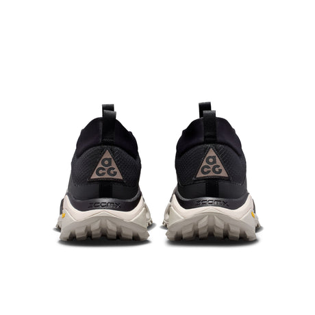 A pair of black and dark gray trail running shoes shown from the rear, featuring a black mesh upper, a gray triangular ACG logo on the heel, and a chunky off-white sole with 'ZOOMX' branding. - Nike ACG Zegama Hike Shoes (Men's) - Black/Ironstone-Cream II