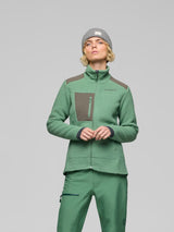 A model wearing a green fleece zip-up jacket with brown shoulder and chest panels, matching green pants, and a gray beanie, photographed against a solid gray studio background. - Norrøna Trollveggen Warm3 Jacket (Women's) - Dark Ivy