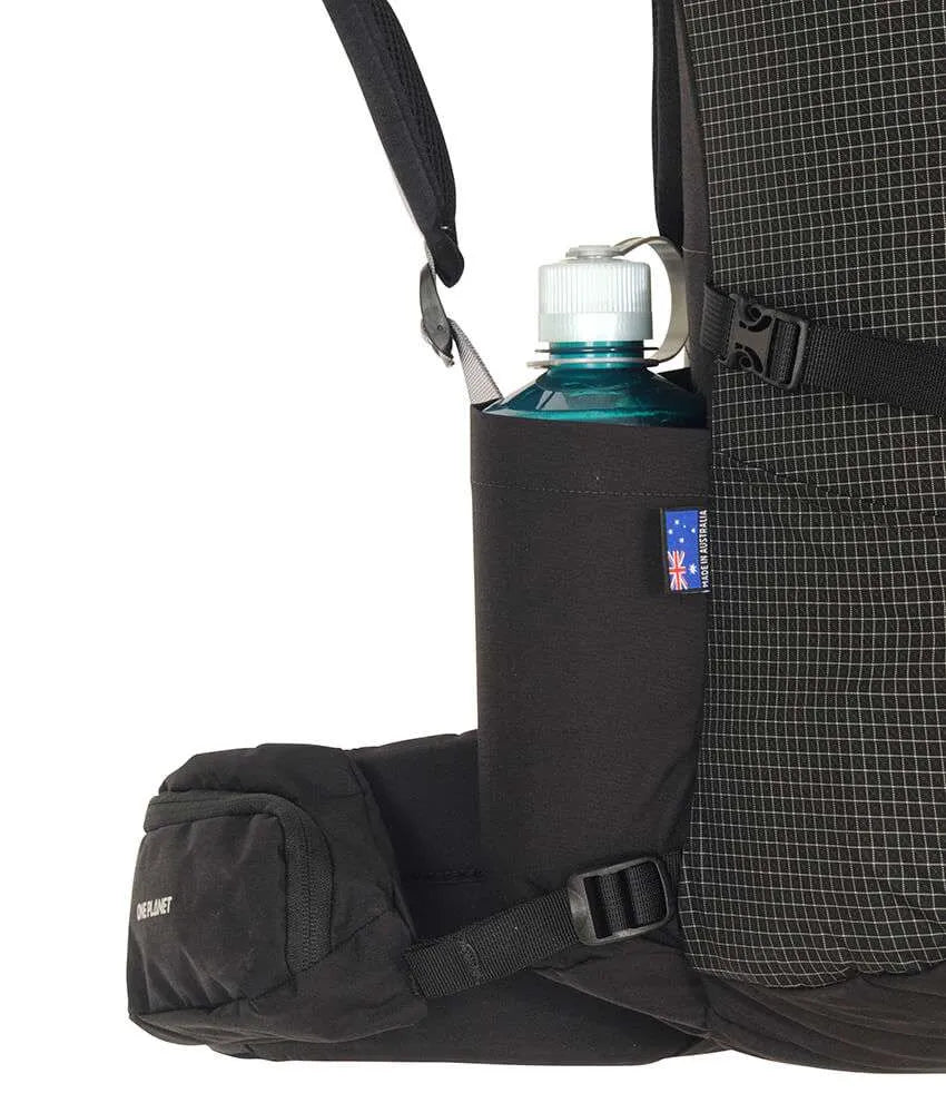 Close-up of a black backpack side pocket holding a dark blue water bottle with a white cap, showing the backpack's grid-patterned fabric and black straps against a white background. - One Planet Extrovert 55L Pack - Black