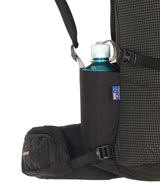 Close-up of a black backpack side pocket holding a dark blue water bottle with a white cap, showing the backpack's grid-patterned fabric and black straps against a white background. - One Planet Extrovert 55L Pack - Black