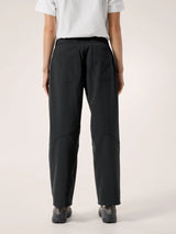 Rear view of a person wearing loose black trousers with a white short-sleeve top and dark shoes, photographed against a plain light beige studio background. - Arc'teryx Nia Pants (Women's) - Black