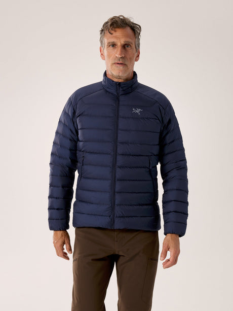 Man wearing a blue puffer jacket with a brand logo on a light gray background - Arc'teryx Cerium Jacket (Men's) - Black Sapphire
